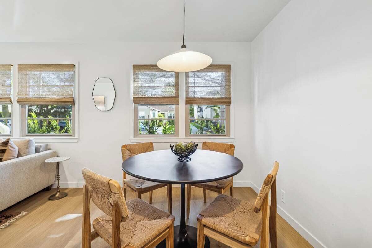 Un coin repas avec une table ronde, six chaises en osier et un luminaire suspendu.