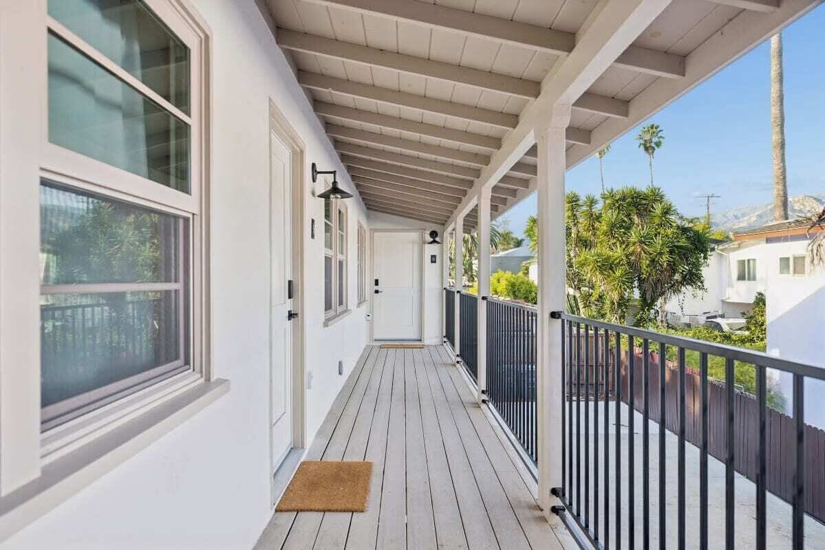 A covered balcony with a wooden floor, white walls, and a black railing.