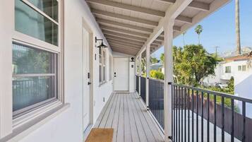 A covered balcony with a wooden floor, white walls, and a black railing.