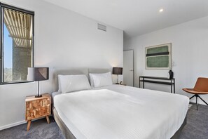 Een moderne hotelkamer met een groot bed, twee nachtkastjes met lampen, een stoel, een bureau en een groot raam.