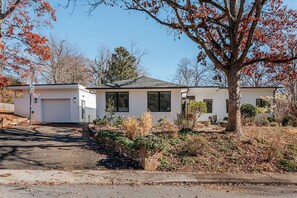 Ein eingeschossiges Haus mit Garage, Vorgarten und Baum sowie einer Auffahrt.