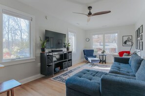 Ein modernes Wohnzimmer mit einer großen Couch, einem Fernseher auf einer schwarzen Unterhaltungsecke und einem Deckenventilator.