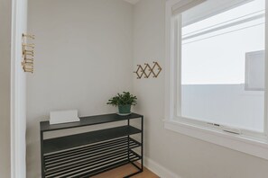 Ein Teil eines Raumes mit einem schwarzen Metallregal, einem weißen Gegenstand darauf und einer grünen Pflanze. Es gibt dekorative Wandhaken und ein Fenster mit Blick.