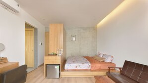 Una habitación pequeña con cama, escritorio, refrigerador, banco y sofá.