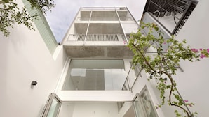 Un edificio moderno con fachada de vidrio, balcones y un pequeño jardín con flores rosadas.