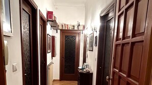 A hallway with tiled flooring, wooden doors, and a small table with items on it. - Central and spacious apartment 100m from the sea! (Alassio)