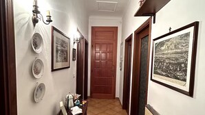 A narrow hallway with a wooden door at the end, flanked by walls with framed pictures and decorative plates. - Central and spacious apartment 100m from the sea! (Alassio)