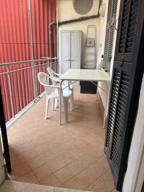 A small balcony with a white table and two white chairs, a red fence, and a white cabinet.