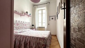 A bedroom with a bed, a window, a radiator, and a wall with framed pictures. - Central and spacious apartment 100m from the sea! (Alassio)