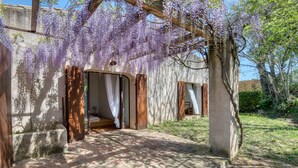 Un'area esterna riparata con pavimento in cemento, porte in legno e un albero con fiori viola.