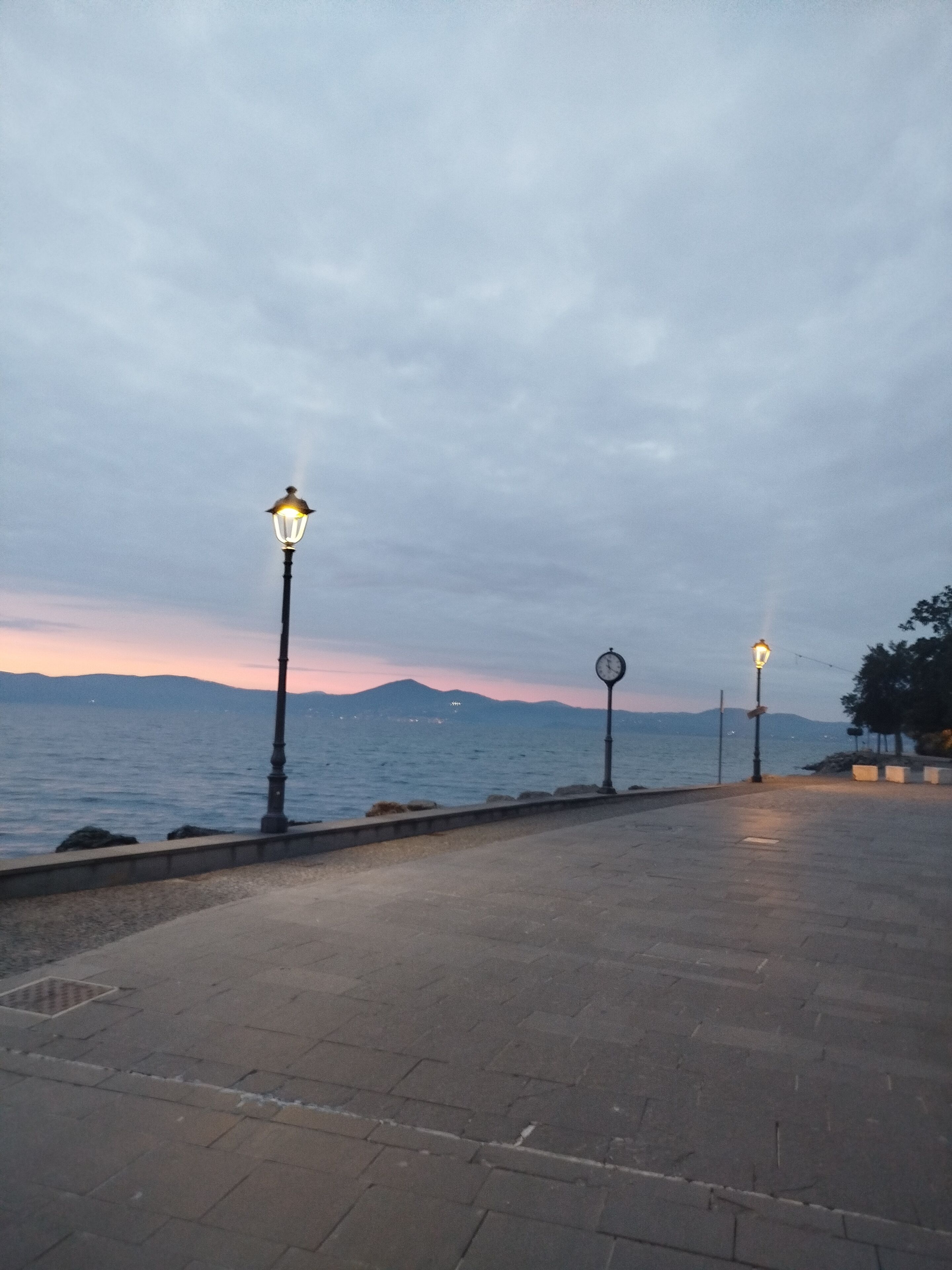 Una passeggiata lungomare con lampioni e un orologio.