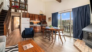 A modern kitchen with wooden cabinets, a dining area with a round table, and a view of the outdoors through a sliding glass door. - Serene Northern Michigan 3-bedroom townhome near Boyne Mountain and Gaylord (Gaylord)