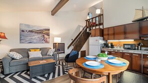 A modern living room with a sofa, coffee table, and a dining area with a wooden table set for four. A staircase leads to an upper level. - Serene Northern Michigan 3-bedroom townhome near Boyne Mountain and Gaylord (Gaylord)