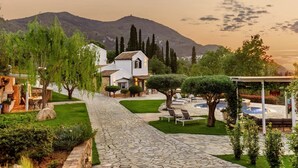Un vialetto in pietra conduce a una casa bianca con un giardino, una piscina e una montagna sullo sfondo.