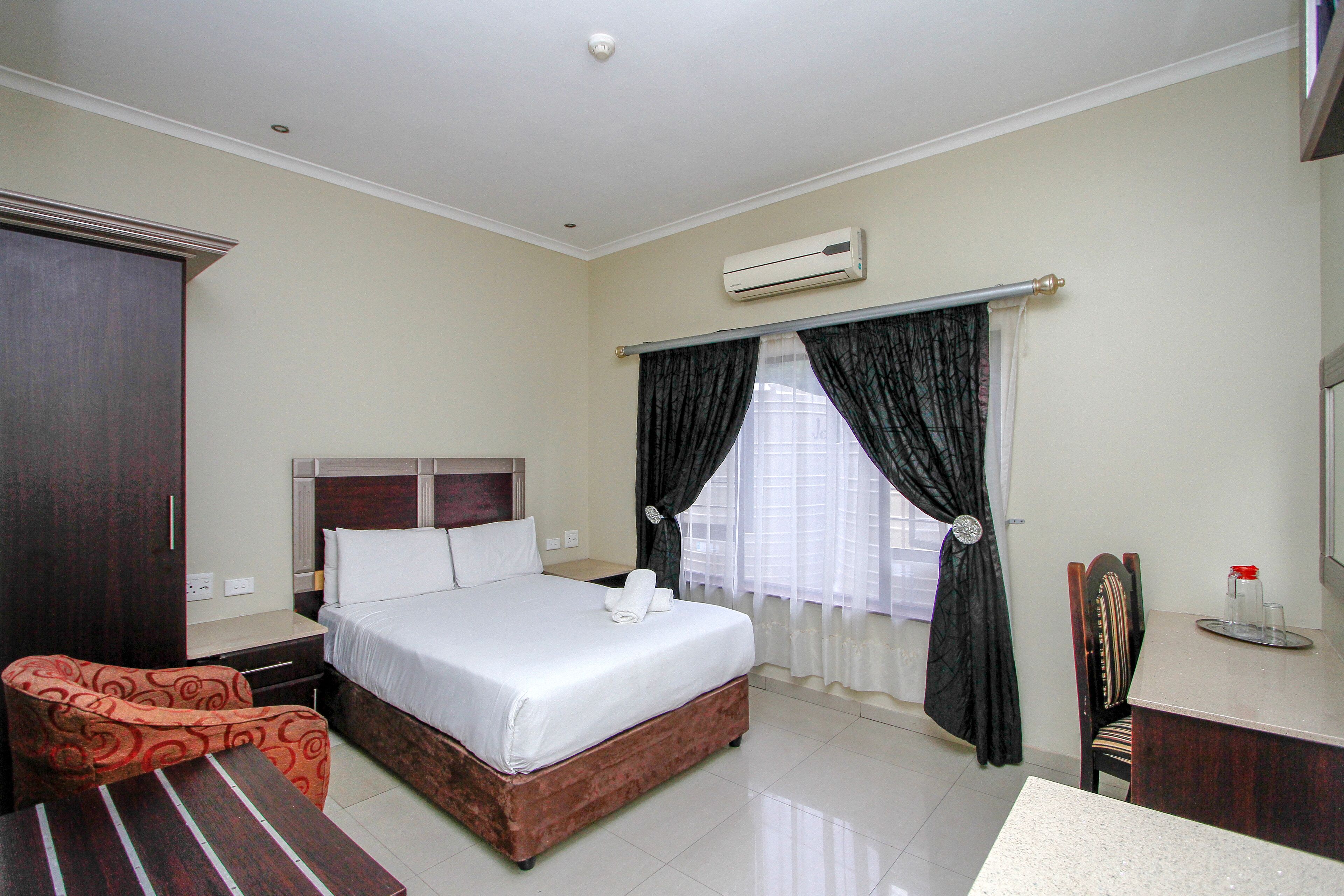 A hotel room with a bed, a desk, a chair, and a wardrobe.