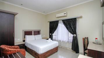 A hotel room with a bed, a desk, a chair, and a wardrobe.