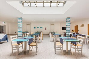 Un vaste espace dédié à la salle à manger, avec des tables et des chaises, un plafond haut agrémenté de lucarnes et des œuvres d’art décoratives sur les murs.
