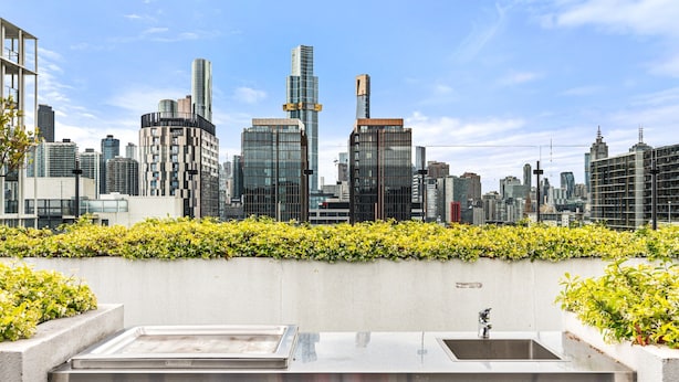 A rooftop terrace with a city skyline view, a concrete wall with greenery, and a metal sink. - South Melbourne Apartment With Gym Access (Melbourne)