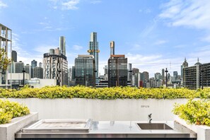 Una terrazza sul tetto con vista sullo skyline della città, un muro in cemento con vegetazione e un lavandino in metallo.