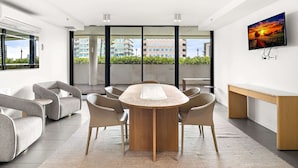 A modern meeting room with a round table, comfortable chairs, a large window, and a mounted TV. - South Melbourne Apartment With Gym Access (Melbourne)