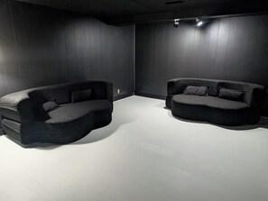 Two modern, dark-colored sofas in a minimalist room with wooden panel walls and a plain floor.
