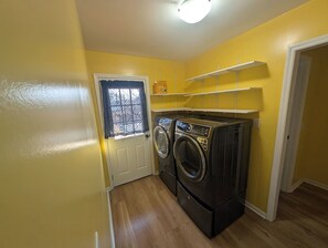 A laundry room with two washing machines, a door with a window, and a shelf above the machines.