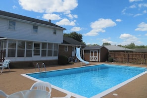 A rectangular swimming pool with a slide, surrounded by a patio with chairs and a covered area. - 5BR Home, Pool + Game Room | Sleeps 16+ (Evansville)