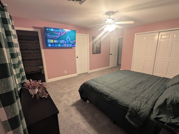 A bedroom with a bed, a ceiling fan, a TV on the wall, and a closet.