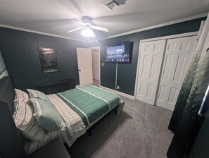 A bedroom with a bed, a ceiling fan, a TV, and a door. - 5BR Home, Pool + Game Room | Sleeps 16+ (Evansville)