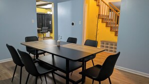A conference room with a long table and six chairs, a small vase with flowers, and a staircase leading to a landing. - 5BR Home, Pool + Game Room -- Sleeps 16+ (Evansville)