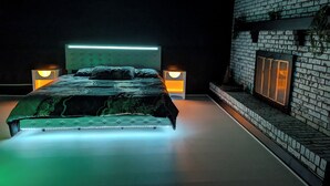 A modern bedroom with a large bed, two bedside lamps, and a brick wall with a fireplace. - 5BR Home, Pool + Game Room -- Sleeps 16+ (Evansville)