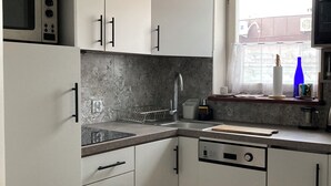 A modern kitchen with white cabinets, a microwave, a dishwasher, and a window with a view of the outside. - A cozy 46m² apartment in a historic tenement house, Great location! (Kraków)
