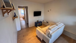Una sala de estar con sofá, televisor y piso de madera.