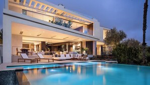 Ein modernes, zweistöckiges Haus mit Swimmingpool, Sitzgelegenheiten im Freien und einem gut beleuchteten Innenraum.