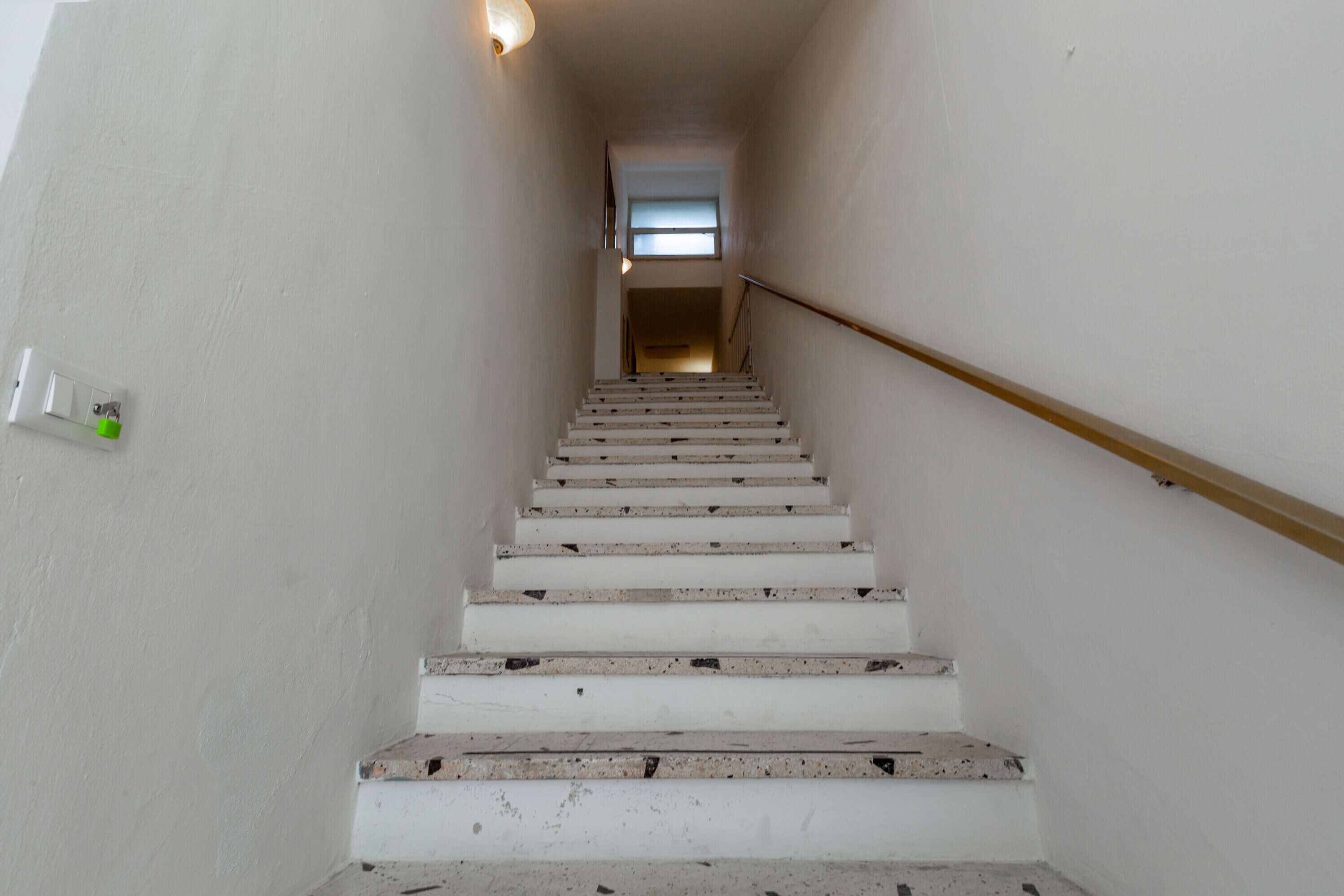 Uma escadaria com degraus brancos e corrimão, que leva a um patamar com uma janela.
