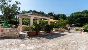Un espacio al aire libre empedrado con pérgola, plantas en macetas y un muro de piedra.