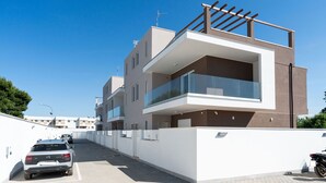 Un immeuble résidentiel moderne à plusieurs étages, doté de balcons, d’un espace de stationnement et surplombant un ciel bleu dégagé.