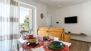 Un coin repas avec une table dressée pour quatre personnes, un canapé, un téléviseur fixé au mur et une fenêtre avec des rideaux.
