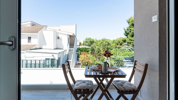 Un balcon avec une table et des chaises, un vase de fleurs et une vue sur des bâtiments et de la verdure.