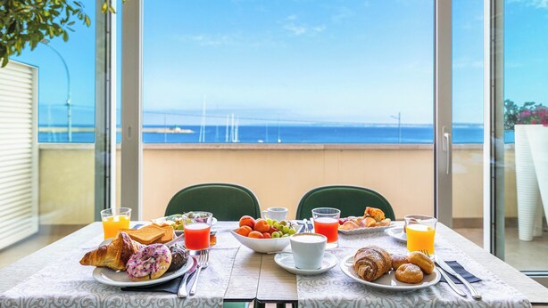 Une table de petit-déjeuner avec vue sur la mer, un balcon et un coin repas avec des chaises et une nappe.