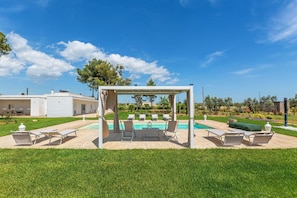 A pool area with a pergola, lounge chairs, and a clear blue sky. - Villa Surya by Perle di Puglia (Ugento)