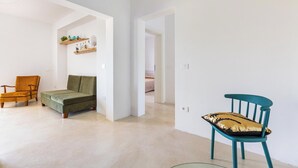 Ein geräumiges Wohnzimmer mit einem grünen Sofa, einem Holzstuhl und einem blaugrünen Sessel mit Zierkissen.
