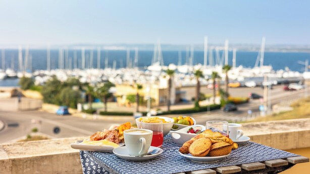 Una mesa con alimentos para el desayuno y vista hacia un puerto deportivo.