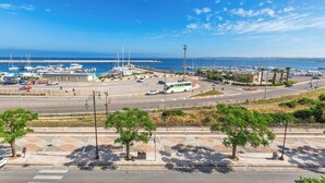 Un puerto deportivo con barcos, una carretera con vehículos y un cielo azul despejado.