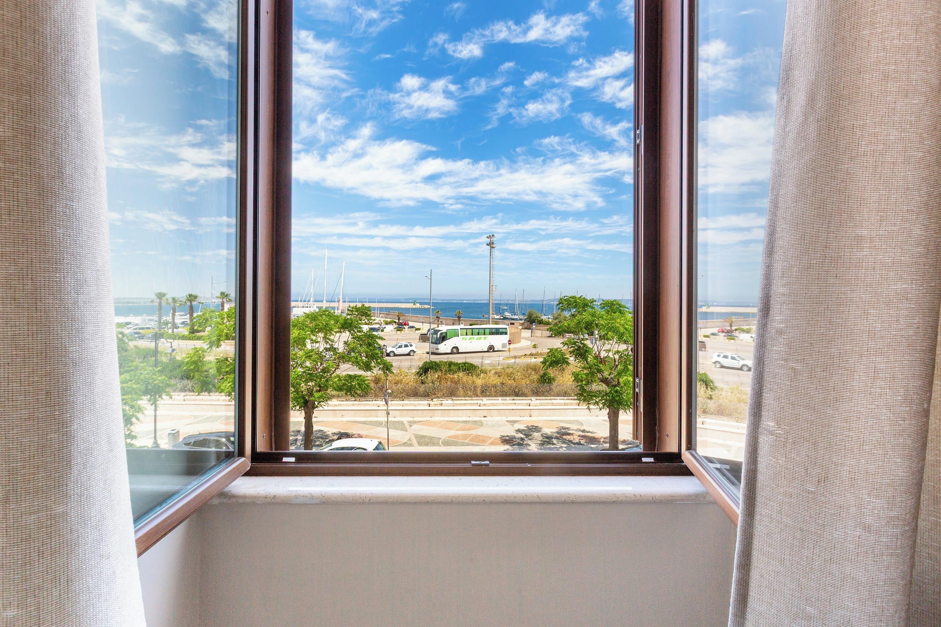 A window with a view of a parking lot, trees, and a clear sky.