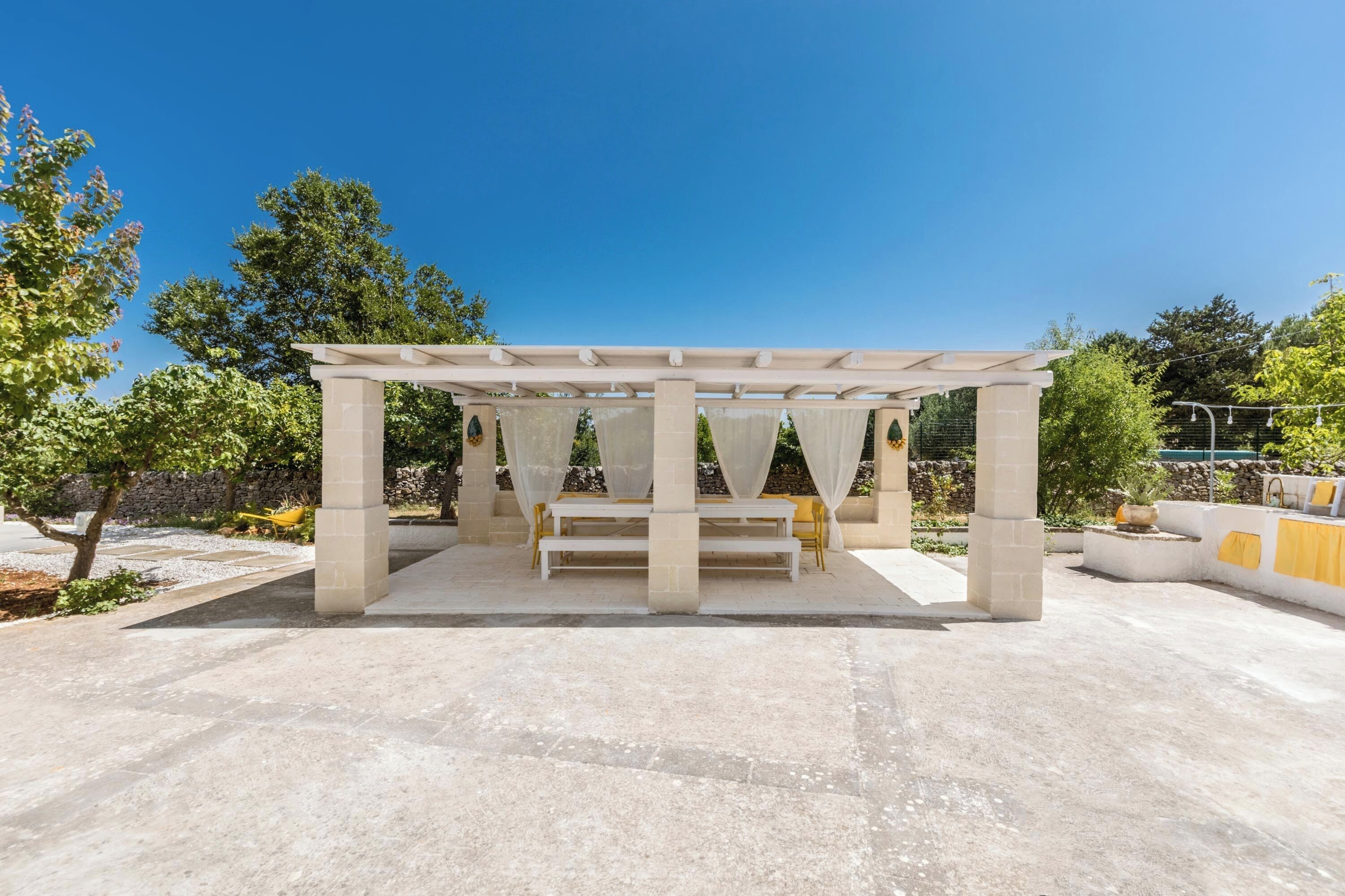 Un espace extérieur aménagé avec une pergola, des piliers en pierre et des bancs, offrant ainsi un coin salon abrité.