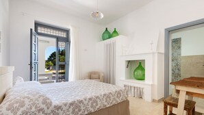 Ein Schlafzimmer mit einem Bett, einem Fenster mit Vorhängen, einem kleinen Tisch und zwei grünen Vasen auf einem Regal.