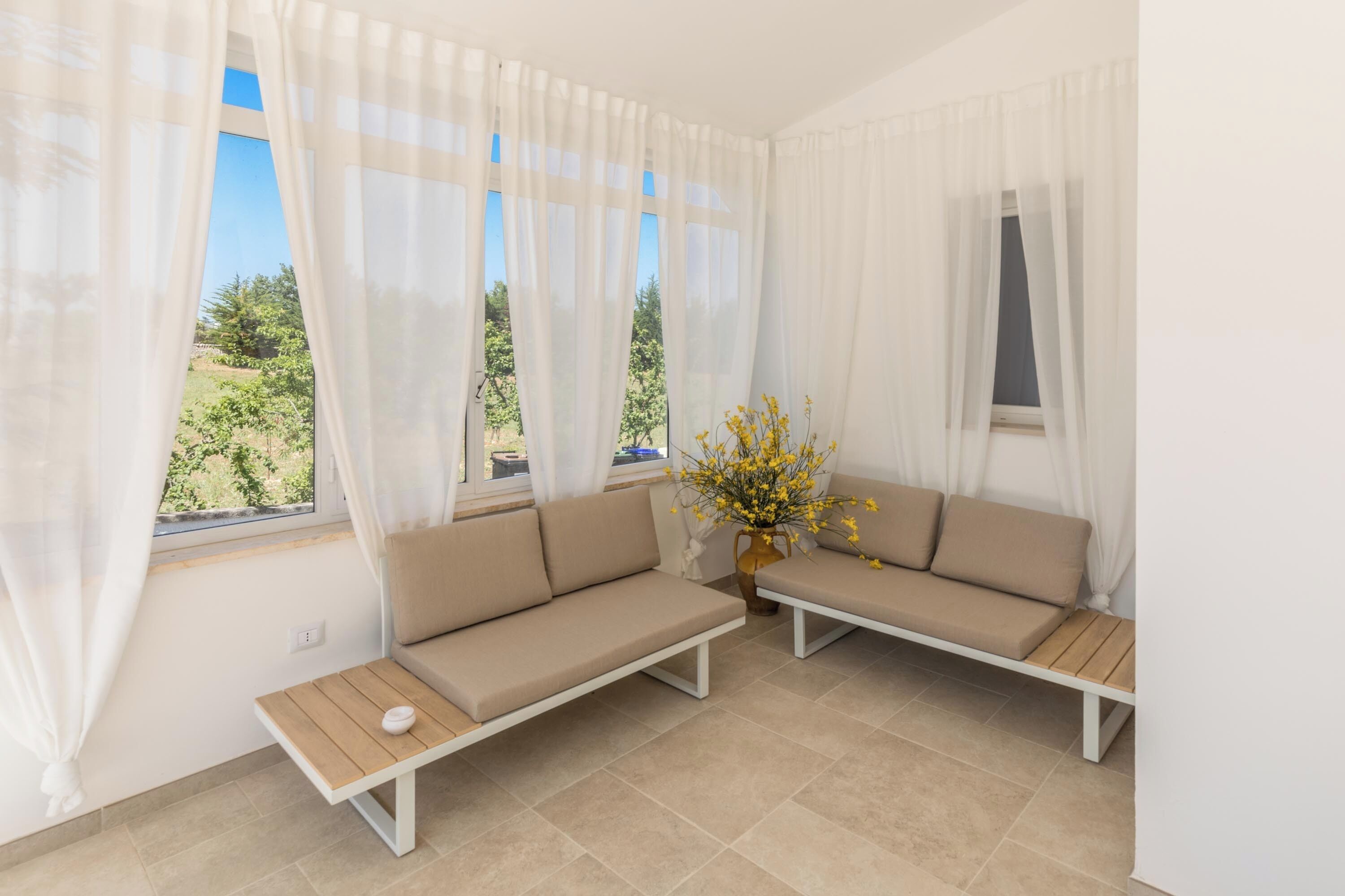 Una habitación con dos sofás beige, una mesita de madera y un florero con flores amarillas.