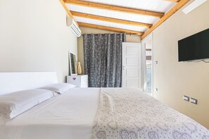 Ein Schlafzimmer mit einem Bett, einem an der Wand montierten Fernseher und einem Fenster mit Vorhängen.