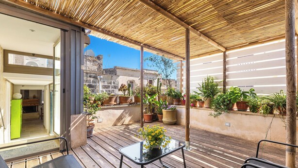 Eine überdachte Terrasse mit Holzfußboden, einem Glastisch und einer Blumendekoration, sowie Blumentöpfe.